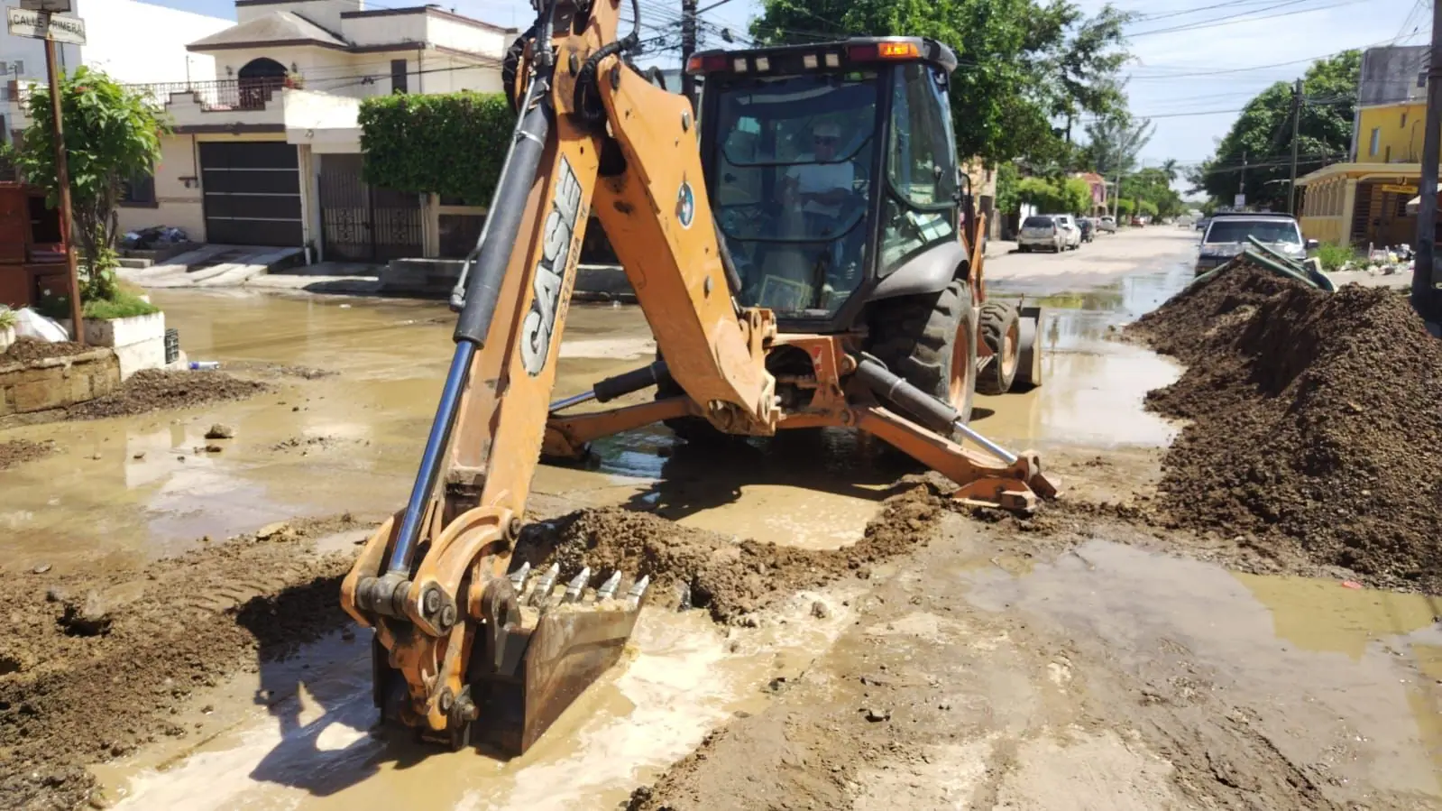 Retroexcavadora Case con el cucharón dentro de una zanja inundada en una calle urbana
